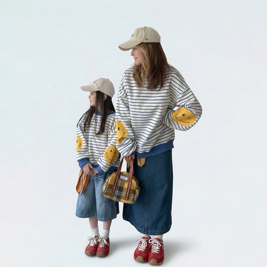 Mother and daughter in matching mommy and me outfits wearing blue striped smiley face sweatshirts.
